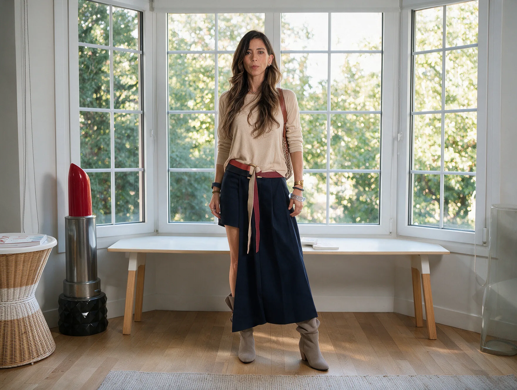 Daniela Peñaloza en estilo creativo: jersey fino, falda azul marino asimétrica con abertura, cinturón de cinta anudado, pulseras de colores y botas de ante
